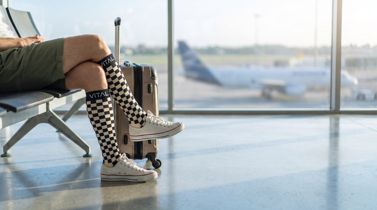 Checker knee-high compression socks with olive shorts and white sneakers, airport seat beside a silver suitcase