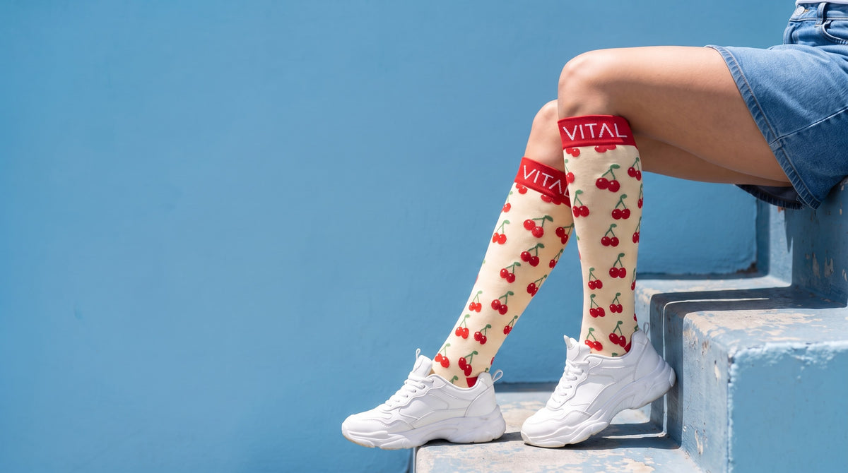 Cherry Pop knee-high compression socks, chunky white sneakers, legs angled down blue painted steps